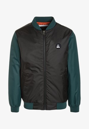Veste bomber noire et vert foncé avec fermeture éclair à l'avant, poignets et col côtelés, et un petit écusson rond sur la poitrine.
