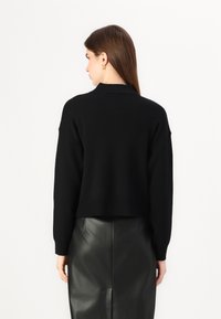Svart cropped genser med lange ermer, ribbestruktur og en subtil krage, parret med et høytlivs svart skinnskjørt.