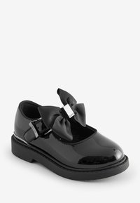 Schwarze Lacklederschuhe mit runder Zehenform, Riemenverschluss und großem strukturiertem schwarzen Schleifenakzent. Dicke Gummisohle mit leichtem Absatz.