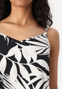 Top sans manches noir et blanc avec un col en V et un motif de feuilles tropicales, doté de fines bretelles et d'un tissu texturé.