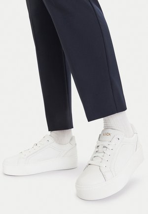 Białe skórzane trampki o teksturowanym wykończeniu, z grubą gumową podeszwą i złotym logo "LSCK". Połączone z granatowymi spodniami i białymi skarpetkami.