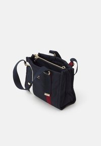 Granatowa nylonowa torba z złotymi okuciami, dwoma zapinanymi na zamek komorami oraz czerwono-białymi paskami. Regulowane paski dla wygodnego noszenia.