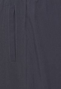 Granatowy materiał o gładkiej fakturze, z poziomą kieszenią i kontrastującym białym przeszyciem wzdłuż krawędzi.