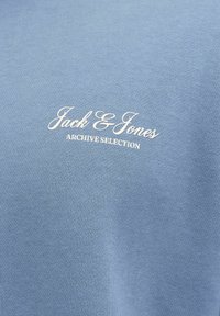 Lyseblå genser med teksturert strikket stoff og et hvitt trykt logo som sier "Jack & Jones ARCHIVE SELECTION."