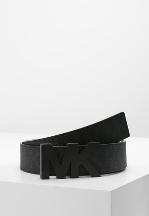 Czarny skórzany pasek z subtelnym wzorem tekstury i dużą czarną klamrą z logo „MK”, prezentowany na białej powierzchni na jednolitym tle.