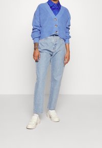 Ljusblå stickad kofta med tre knappar, ihop med ljusblå högmidjade jeans och krämfärgade loafers. Slät textur, avslappnad passform.