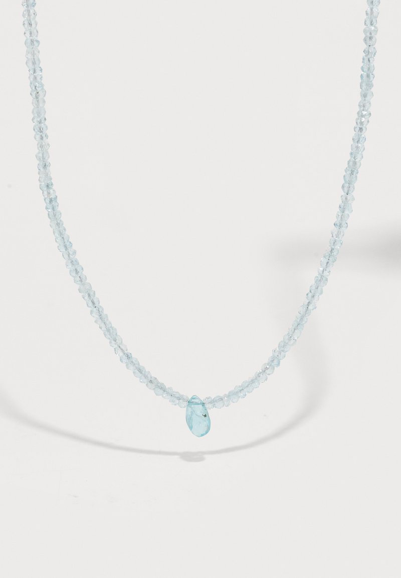 Sofistikerad halsband med ljusblå fasetterade pärlor och en central droppformad pendant, presenterad mot en enfärgad vit bakgrund.