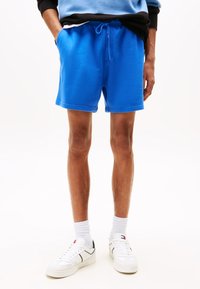 Blue cotton shorts with an elastic waist and drawstring, featuring side pockets. Paired with white sneakers and gray socks.