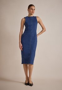Rochie midi din denim de culoare albastru închis, cu un design ajustat, decolteu rotund, detalii vizibile de cusătură și fără mâneci. Asortată cu tocuri negre.