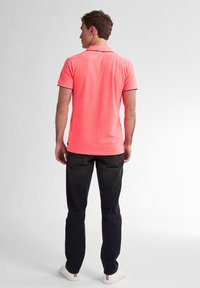 Polo à manches courtes en corail vif avec un col contrastant, associé à un jean foncé et des baskets blanches. Coupe ample et texture lisse.