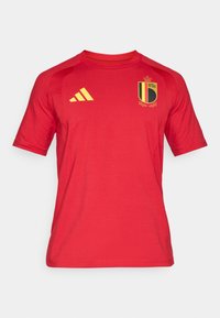 Rdeča športna majica iz lahkega blaga. Na njej je rumen logotip Adidas, belgijski državni grb na prsih, kratki rokavi in okrogel ovratnik.