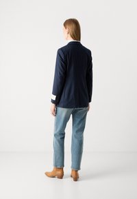 Navy pinstripe blazer with tailored design, white cuff accents, paired with light blue straight-leg jeans and tan ankle boots.