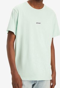 Mint green cotton t-shirt with short sleeves and a crew neck. Features a black "LEVI'S" logo printed on the chest. Simple design.