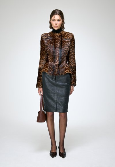 Femme portant une veste en fourrure imprimé léopard marron, une jupe crayon en cuir noir, des collants transparents noirs, des talons noirs et tenant un sac à main marron.