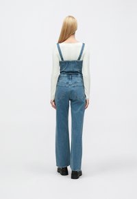 Τζιν φορμάκι σε ανοιχτό μπλε με ρυθμιζόμενους ιμάντες, σχέδιο με φαρδύ πόδι και εφαρμοστή μέση. Συνδυασμένο με λευκό μακρυμάνικο τοπ με υφή.