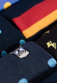 Drie paren sokken: donkerblauw, rood en geel met patronen. Eén heeft een cartoon dierengezicht; de andere hebben stippen en bliksemontwerpen.