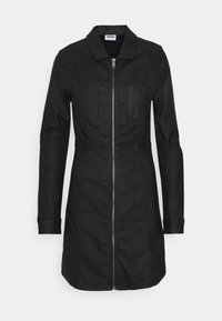 Svart denimklänning med krage, blixtlås fram, två bröstfickor och långa ärmar. Har en figursydd silhuett och slät textur.