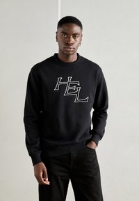 Must black tindiga valge "HEL" kirjutisega, soonikuga ümar kael ja randmed. Kombineeritud mustade pükstega, mudel on keskel neutraalsel taustal.