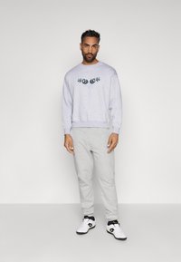 Sweatshirt cinza com gola arredondada e estampa gráfica, combinado com calças de moletão cinza claro e ténis brancos com detalhes pretos.