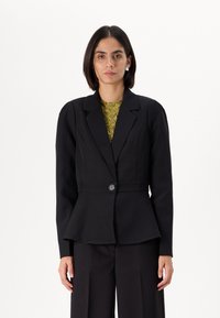 Fekete szabott blézer peplum derékkal, egygombos záródással és strukturált vállakkal. Texturált zöld felső fölött viselve.