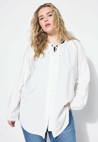 Hvid, langærmet skjorte med knaplukning og afrundet halsudskæring, med snoretræk og afslappet pasform. Bæret med blå denim jeans.