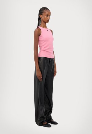 Rosa tettsittende tanktopp med sidesøm-detaljer, paret med løse svarte faux skinnbukser og enkle svarte sko.