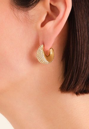 Orecchini tono oro con un design curvo e liscio caratterizzato da una superficie testurizzata adornata con strass trasparenti che riflettono la luce in modo attraente.