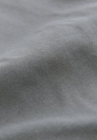 Zbliżenie na gładką, jasnoszarą tkaninę o drobnej dzianinowej fakturze i delikatnych fałdach tworzących miękkie cienie.