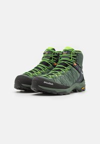 Green hiking boots featuring a textured upper, black rubber toe cap, and bright green laces. The sole includes a distinctive tread pattern.