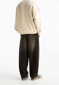 Beżowy, oversize'owy sweatshirt z ribbedowymi mankietami, połączony z czarnymi, denimowymi spodniami typu wide-leg, które mają dwie tylne kieszenie i wyblakłą teksturę.