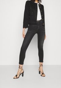 Svart jeansjacka med spetsdetaljer, matchad med högmidjade svarta skinny jeans och svarta sandaler med remmar som har rundade detaljer.