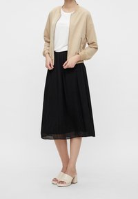 Beige bomberjakke, hvid t-shirt, sort plisseret midinederdel og beige mule med blokhæl. Glat stof, afslappet pasform og lodrette linjer.