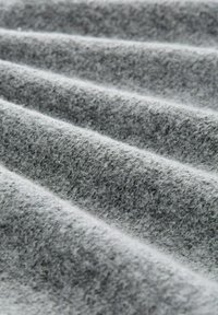 Grauer texturierter Stoff mit weichen, flauschigen Fasern in einem drapierten Muster, das unterschiedliche Grautöne und subtile Tiefe durch Falten aufweist.