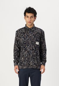 Camică cu model paisley de culoare bleumarin, cu mâneci lungi, cu un închidere butonată și o etichetă mică pe piept. Textură de țesătură moale.
