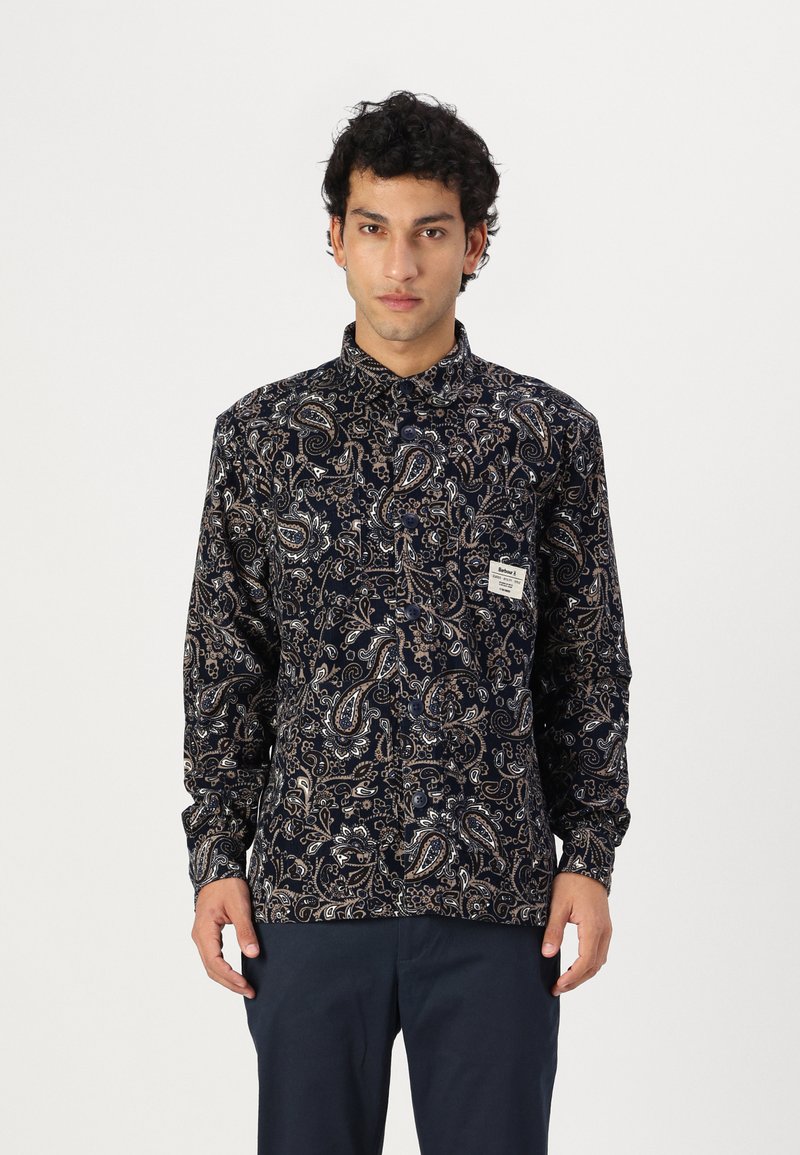 Camică cu model paisley de culoare bleumarin, cu mâneci lungi, cu un închidere butonată și o etichetă mică pe piept. Textură de țesătură moale.