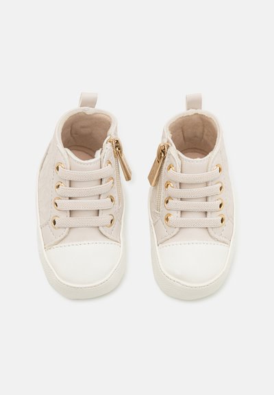 Helle beige Kindersneaker mit einer strukturierten Oberseite, weißer Gummispitze, goldenen Akzenten und Schnürung vorne sowie einem seitlichen Reißverschluss.