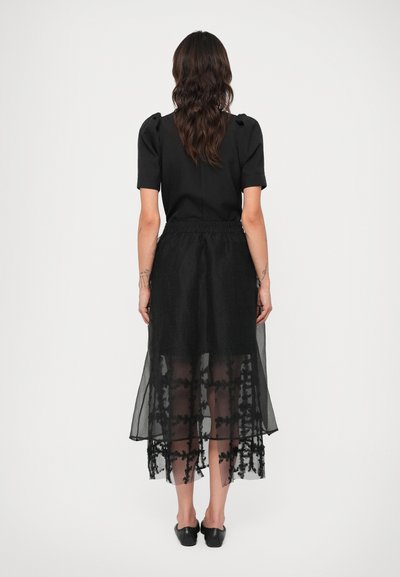 Melnas kleitas ar pieguļošu augšdaļu un īsām piedurknēm, kuras apakšā ir caurspīdīga, slāņota svārku daļa ar ziedu izšuvumu apakšmalā. Lēti melni apavi.