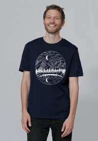 T-shirt bleu marine à manches courtes, présentant une impression circulaire blanche de montagnes, d'arbres et de lunes dans un style de dessin linéaire détaillé.