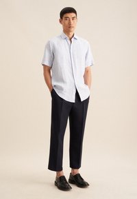 Camicia a maniche corte a righe blu chiaro con bottoni davanti, abbinata a pantaloni larghi blu scuro e scarpe nere stringate.