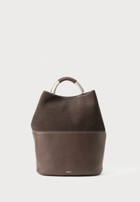 Két színű barna bőr és velúr bevásárlótáska lekerekített fogantyúval, a "Furla" logóval a táska alsó részében, fehér háttérrel.
