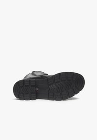 Botte en cuir noir avec une semelle en caoutchouc texturé présentant un motif en zigzag, moulée pour l'adhérence. Le matériel comprend une fermeture éclair sur le côté.