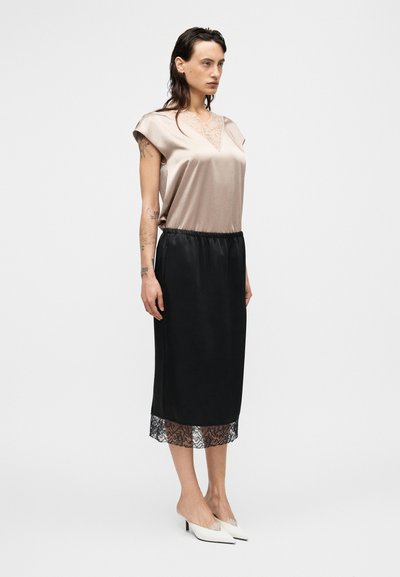 Εκρού σατέν τοπ με V-λαιμόκοψη, συνδυασμένο με μαύρη φούστα με ελαστική μέση και δαντελωτό τελείωμα στο στρίφωμα. Λευκές μυτερές γόβες.