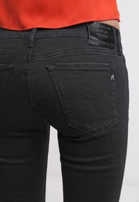 Vaqueros de denim negro con un ajuste ceñido, dos bolsillos traseros con detalles de costura sutil y una etiqueta de cuero de la marca en la cintura.
