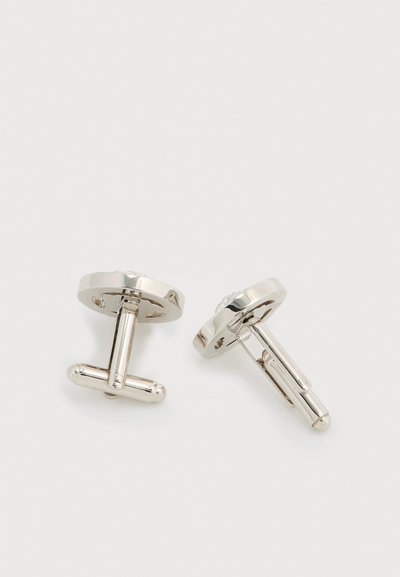 Ασημένιοι μανικετόκουμπες με στρογγυλό σχήμα δίσκου, λεία επιφάνεια και κούμπωμα τύπου T-bar. Μινιμαλιστικός σχεδιασμός χωρίς επιπλέον διακοσμητικά.