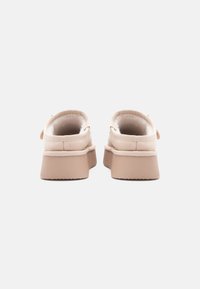 Snygga beige slip-on skor med en mjuk mockaöverkänsla, vadderad insida och en lätt, texturerad gummisula, med en modern, minimalistisk design.