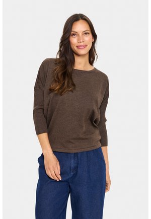 Un pull en tricot marron avec un col rond et des manches trois-quarts, associé à un pantalon en denim bleu ample. Texture lisse, coupe décontractée.