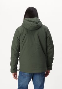 Grøn isoleret jakke med hætte, der har en glat tekstur og elastiske manchetter, parret med blå jeans. Bagview af outfittet.