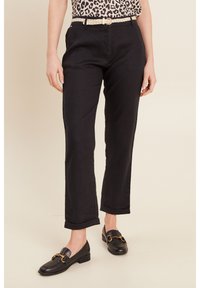 Zwarte linnenbroeken met een getailleerde pasvorm, opgerolde manchetten en een geweven riem. Gecombineerd met zwarte instappers met gouden hardwareaccenten.