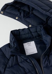 Marineblå quilted jakke med aftagelig hætte, frontlynlås og hvidt plejelabel, der viser størrelse 116 til børn i alderen 5-6 år.