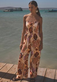 Flerfärgad, mönstrad byxdress med bärande design, som har en draperad midja och vid byxben. Tillverkad av lättviktigt material.